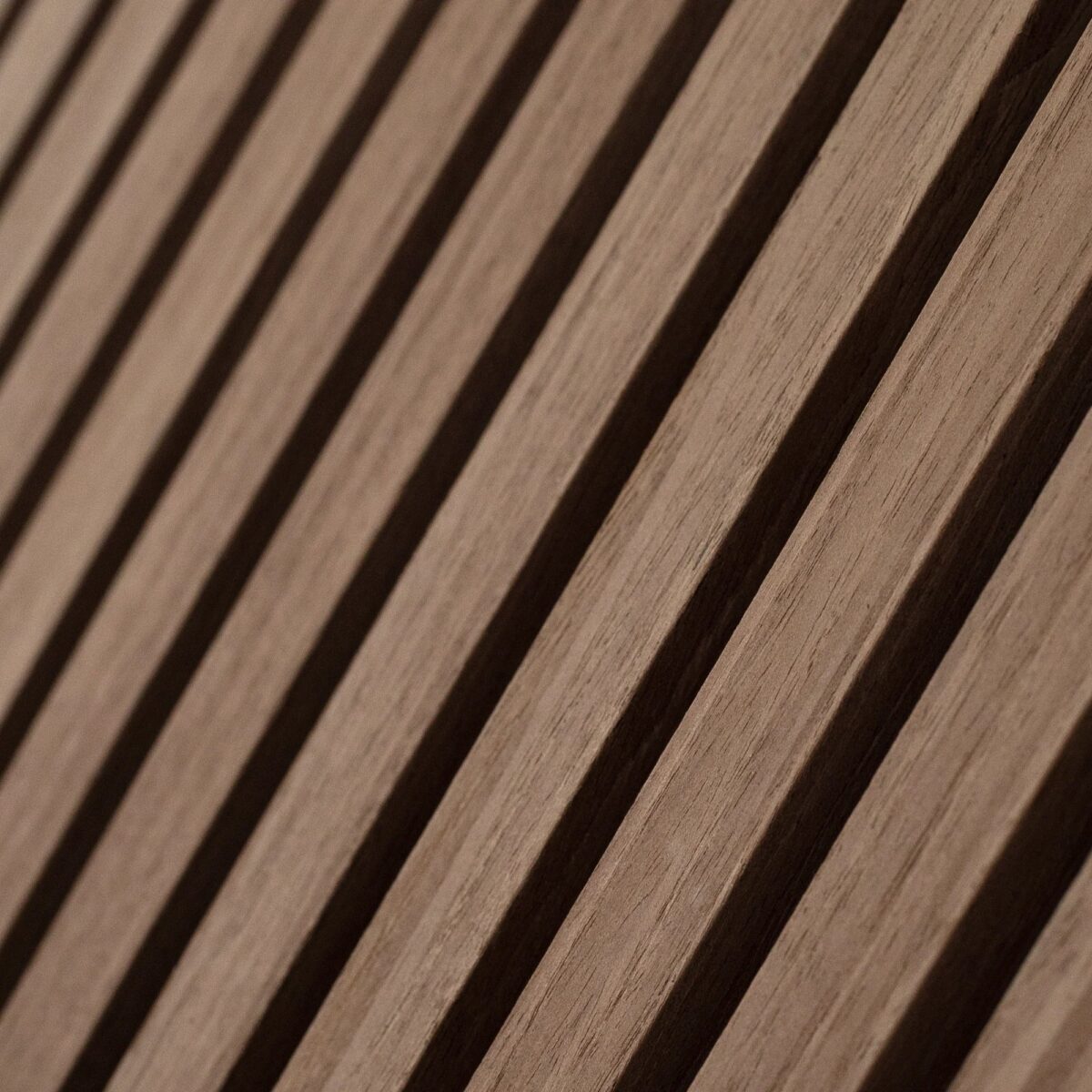Close-up van de Akupanel Eiken Mokka 60 x 60 cm Lattenwand akoestische wandpanelen, met gelijkmatig verdeelde verticale latten in natuurlijk bruin met een gladde afwerking, waardoor een opvallend licht- en schaduwpatroon ontstaat.