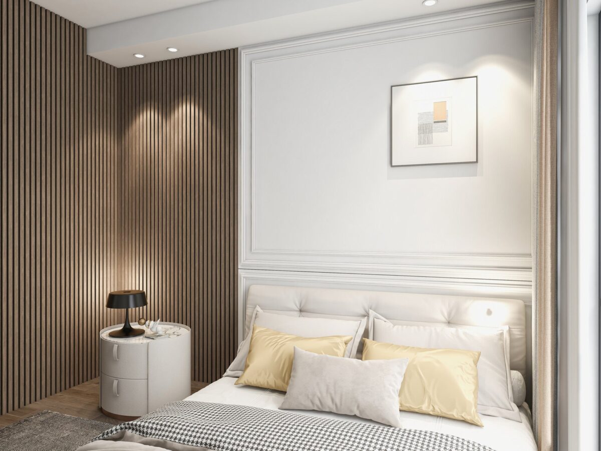 Een moderne slaapkamer heeft een wit bed, gele en witte kussens, een klein rond nachtkastje met een zwarte lamp en een Akupanel Eiken Mokka 270 x 60 cm lattenwand akoestische wandpanelen accentmuur. Boven het bed hangt ingelijste minimalistische kunst; zacht natuurlijk licht vult de kamer.