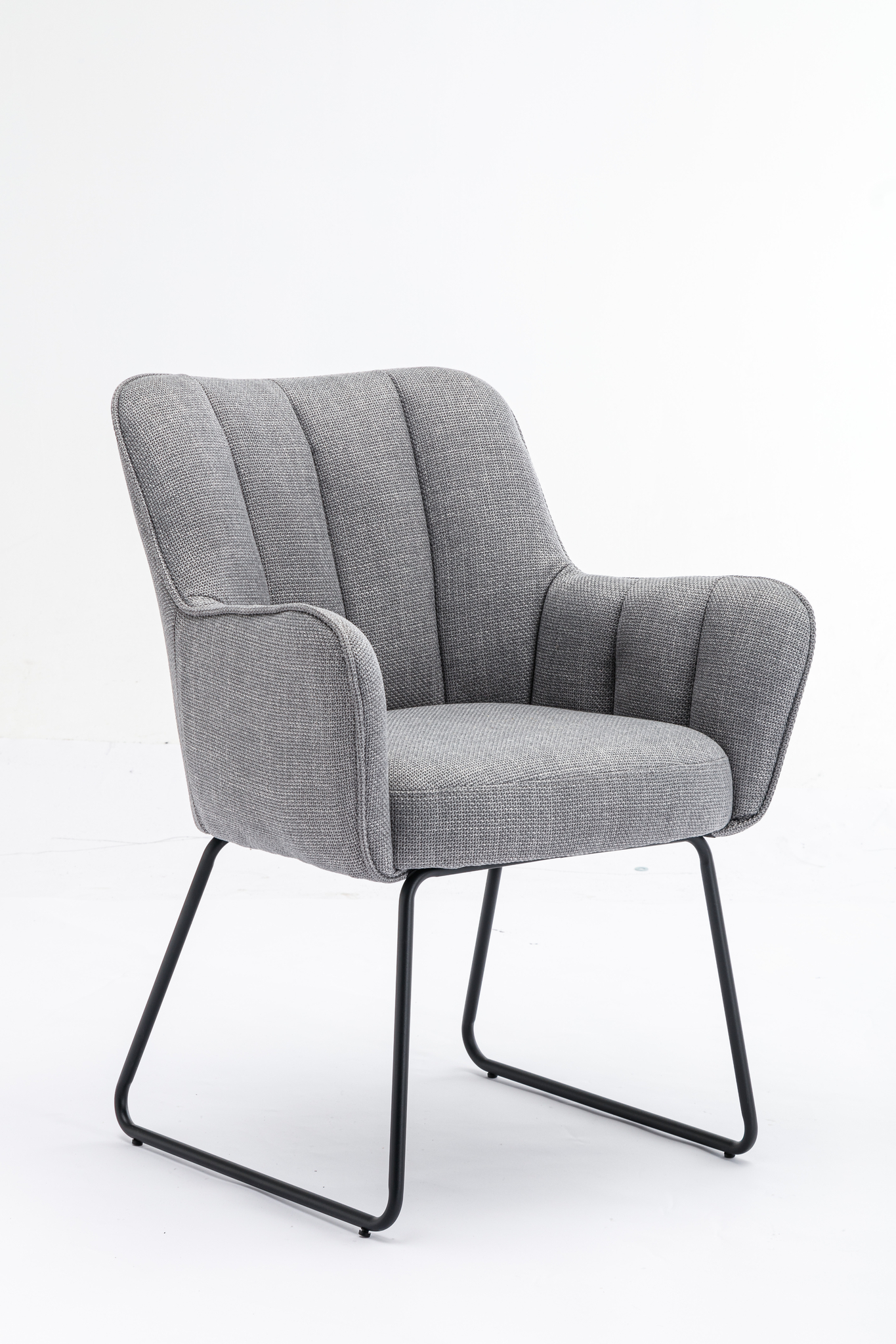 De Stoel Kevin Bjorn Fabric Light Grey is een moderne fauteuil met een gebogen rug en armen, verticale stiksels en zwarte metalen sledepoten, op een effen witte achtergrond.
