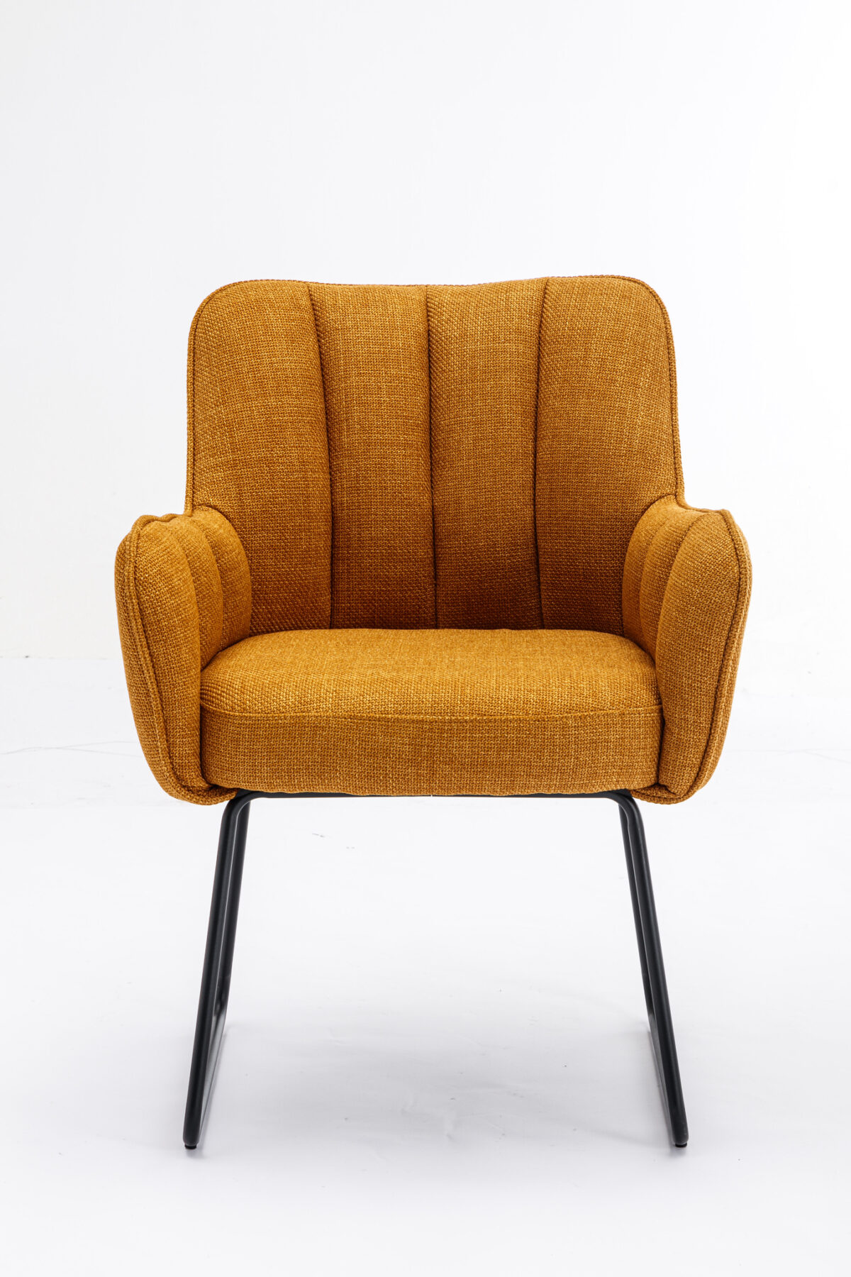 De Stoel Kevin Bjorn Fabric Mustard is een mosterdgele gestoffeerde fauteuil met verticale stiksels, schuine armleuningen en zwarte metalen poten, tegen een effen witte achtergrond.