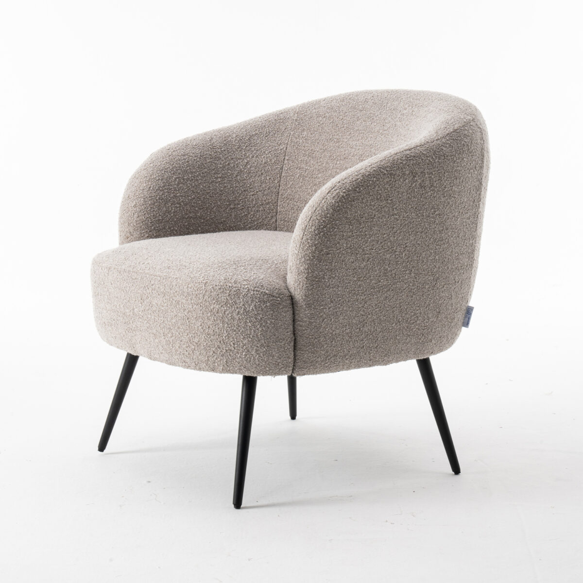 De Laura fauteuil Stof Teddy Natural 01 is een moderne, lichtbeige gestoffeerde fauteuil met een gebogen rugleuning en armleuningen op vier slanke zwarte metalen poten, tegen een effen witte achtergrond.