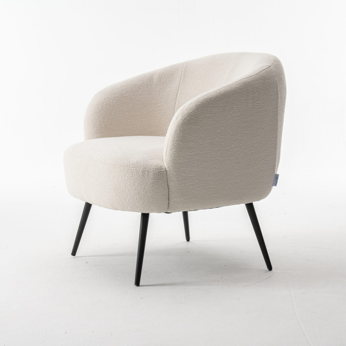 De Laura fauteuil Stof Teddy Ivory 101 is een moderne accentstoel met een afgeronde rugleuning en zitting in gebroken witte teddystof, voorzien van vier slanke zwarte metalen poten, afgebeeld tegen een witte achtergrond.