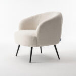 De Laura fauteuil Stof Teddy Ivory 101 is een moderne accentstoel met een afgeronde rugleuning en zitting in gebroken witte teddystof, voorzien van vier slanke zwarte metalen poten, afgebeeld tegen een witte achtergrond.