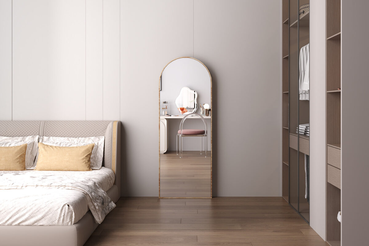 Een moderne slaapkamer heeft een netjes opgemaakt bed, beige en gouden kussens, een houten vloer en de grote Spiegel 'Rosalie' 160x60 Oude eik (1c) gewelfde spiegel die een ijdelheid weerspiegelt. Een open kledingkast met kleding bevindt zich aan de rechterkant.