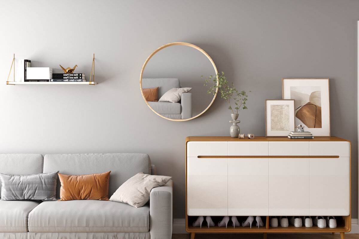 Een moderne woonkamer met een grijze bank, aardetinten kussens, een witte en houten kast, ingelijste kunst, de Spiegel 'Ria' 80x80 Oude eik (1c) spiegel, een vaas met een plant en een gouden plank met boeken op een lichtgrijze muur.