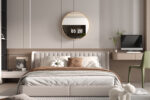 Een moderne slaapkamer met de Spiegel 'Roxy' 80x80 Oude eik (1c) ronde spiegel boven een beige gestoffeerd bed, bruin en wit beddengoed, een aan de muur bevestigd bureau met een computer en een groene stoel.