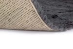 Een close-up van het Merano Charcoal 013 170x230 tapijt toont de donkergrijze, pluizige textuur, gedeeltelijk gevouwen om een beige onderkant met een gestippeld antislippatroon te onthullen.