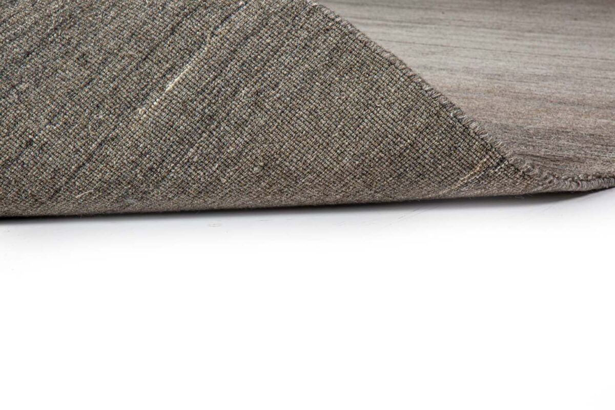 Een close-up toont de hoek van het Portofino Beige 02 200x300 tapijt, opgetild om de onderkant te onthullen, tegen een witte achtergrond.
