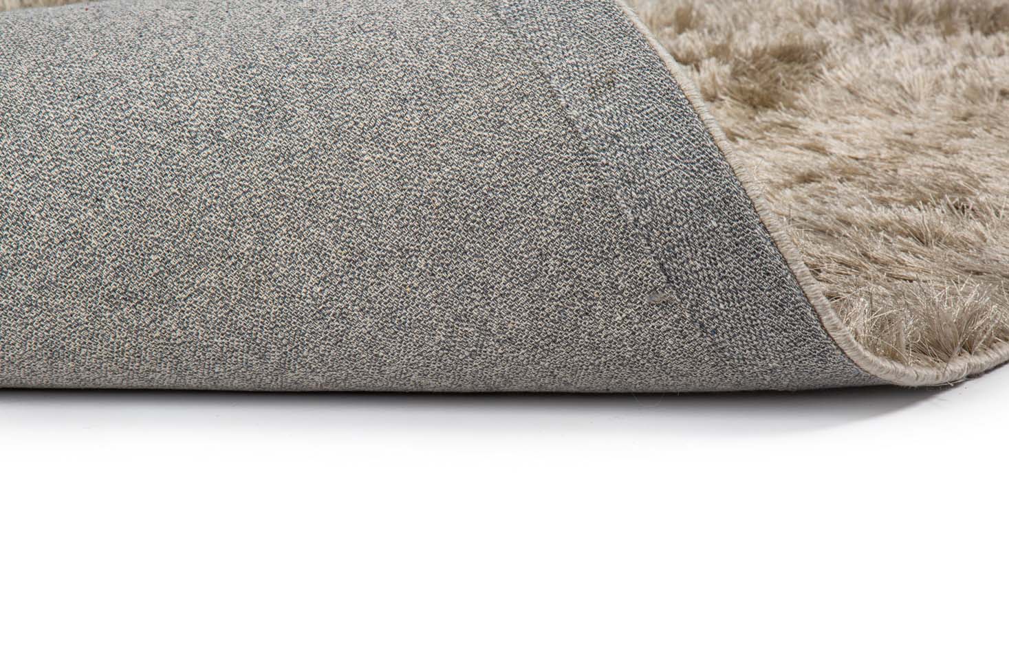 Een close-up van het Arezzo ST Silver 119 170x230 tapijt, gedeeltelijk gevouwen om de grijze stoffen bovenkant en de zacht beige donzige onderkant tegen een witte achtergrond te tonen.