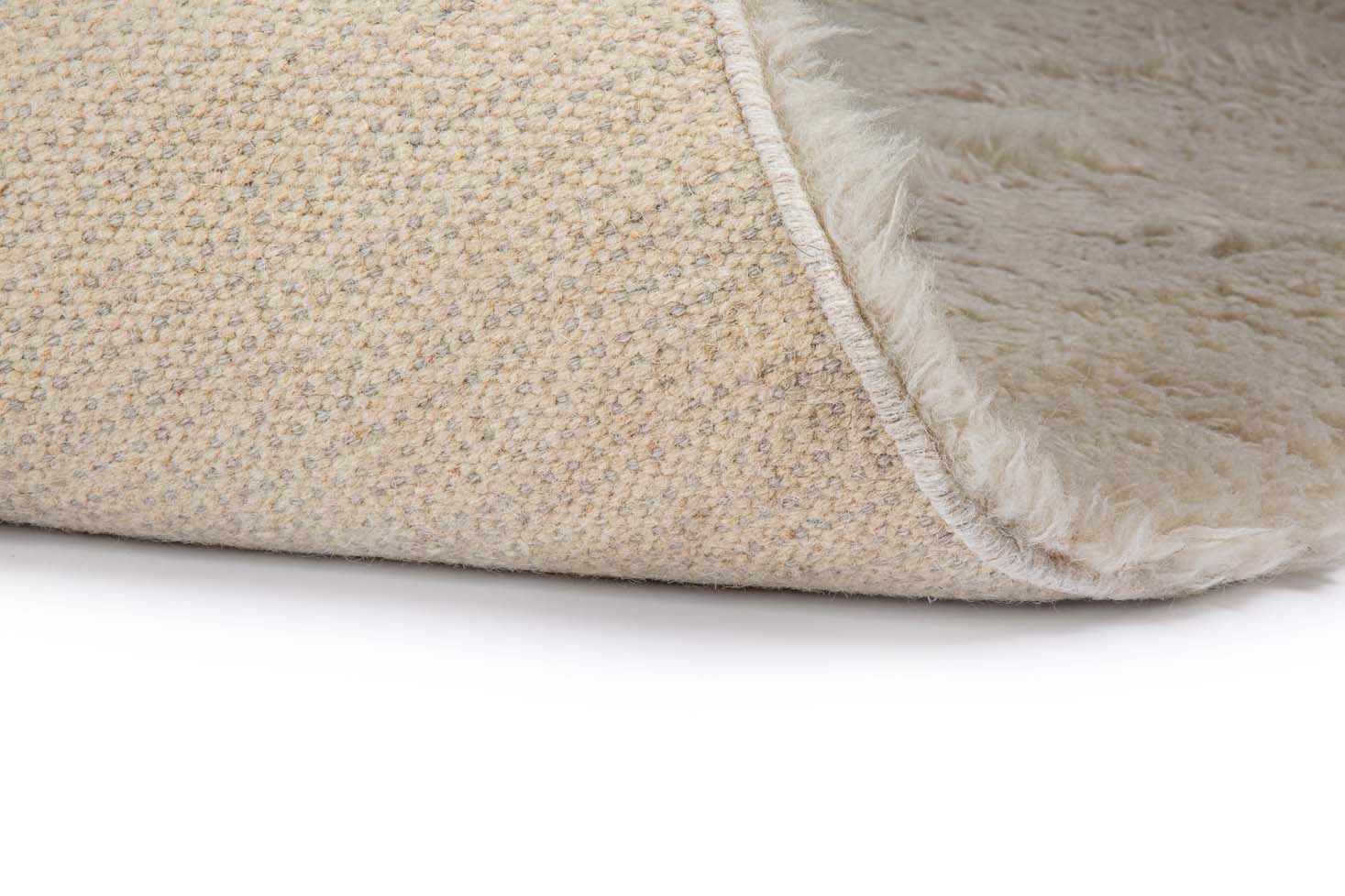 Een close-up van het Merano Silver 012 170x230 tapijt, met de beige geweven bovenkant en de pluizige onderkant, gedeeltelijk gevouwen om beide lagen tegen een witte achtergrond te tonen.