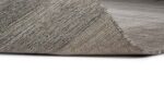 Een close-up van het Portofino Grey 03 170x230 tapijt toont de geweven textuur en het dunne profiel, met een hoek iets omhoog, tegen een witte achtergrond.