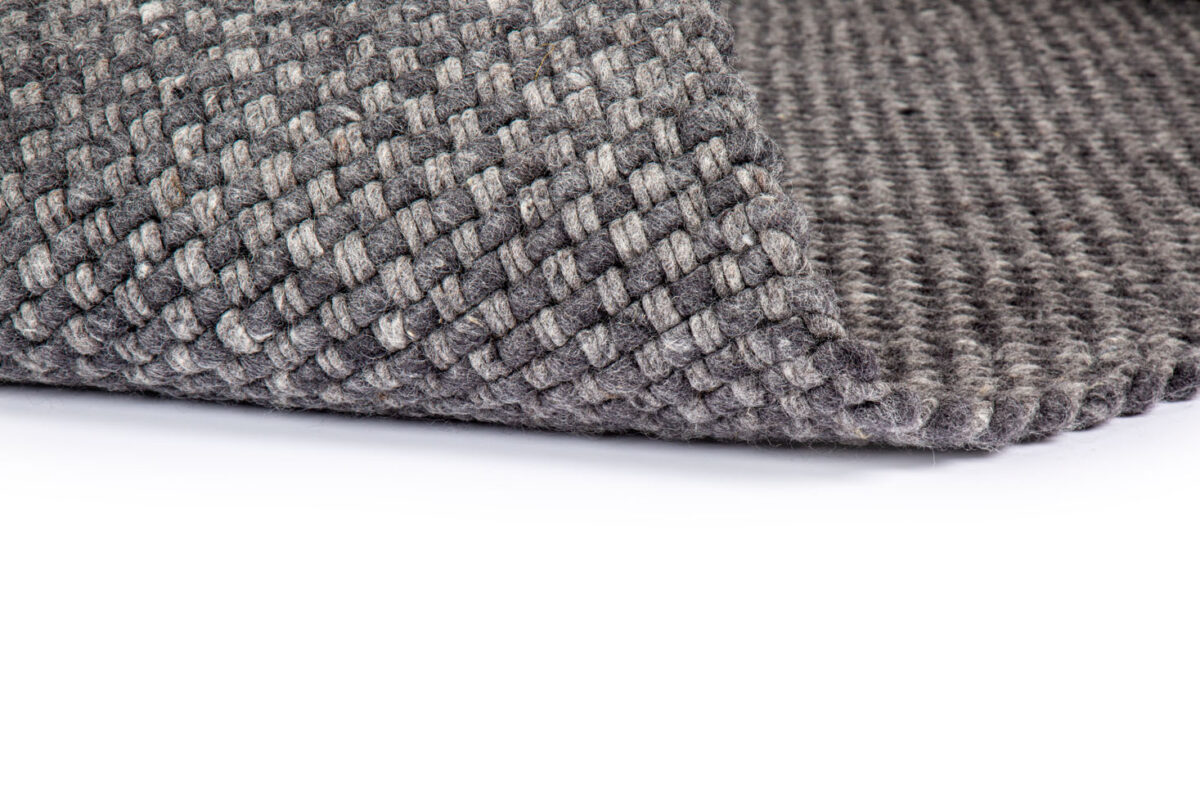 Close-up van de hoek van het Burano Anthracite 614-604 vloerkleed (170x230 cm), met een gestructureerd, geweven mandpatroon in grijs, getoond op een witte achtergrond.