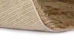 Close-up van het Merano Beige 002 200x300 tapijt met de hoek opgetild, waardoor een gestructureerde, slipvaste onderkant zichtbaar wordt tegen een witte achtergrond.