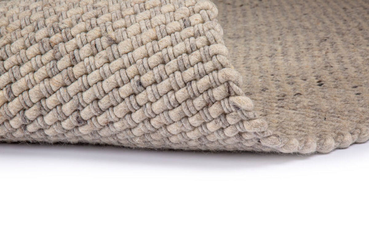 Een close-up van het Burano Light Grey 616-618 200x300 tapijt toont het gestructureerde, grove weefpatroon in een lichtgrijze tint, gedeeltelijk gevouwen om zowel de voor- als achterkant te onthullen tegen een witte achtergrond.