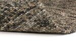 Close-up van de geweven rand van het Verona ST Brown Grey 940 200x300 tapijt in grijze en bruine tinten, gedeeltelijk opgetild om de dikte en het gedetailleerde stiksel op een witte achtergrond te tonen.