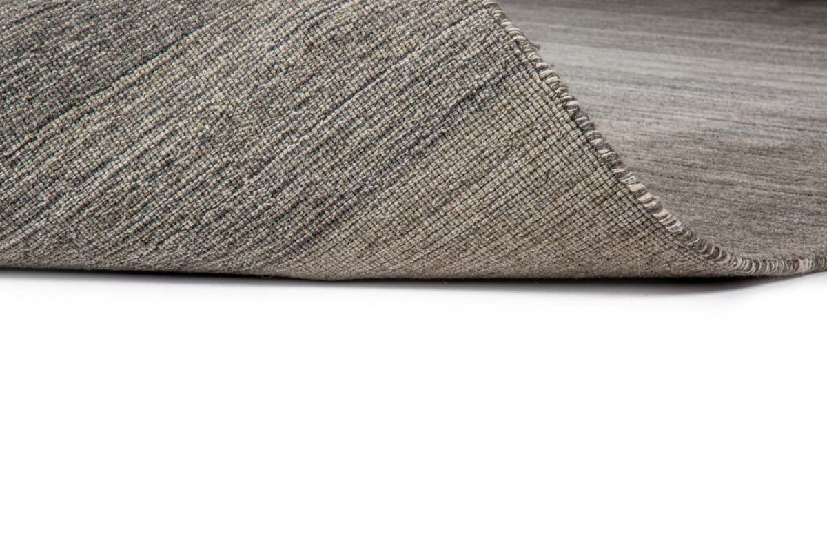 Een close-up van het Portofino Grey 03 200x300 tapijt toont de geweven textuur en dikte, met één hoek iets omhoog tegen een witte achtergrond.
