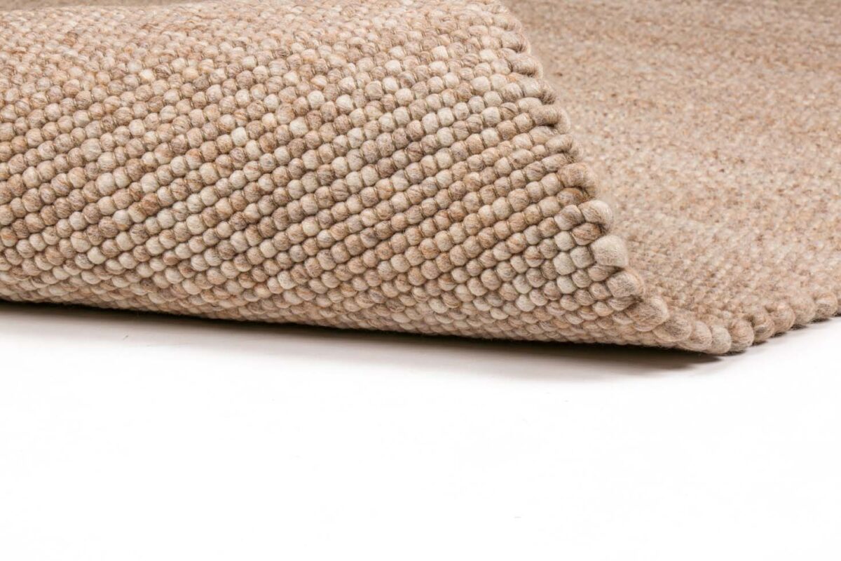 Een close-up van het Verona ST Beige 142 200x300 tapijt toont de dikke, gestructureerde lussen en de opgetilde rand om de onderkant te onthullen, allemaal tegen een witte achtergrond.