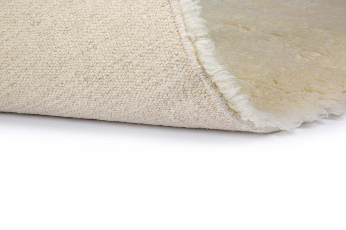 Een close-up van de omgeslagen hoek van het Merano White 011 200x300 tapijt, met de crèmekleurige structuur en zachte onderkant tegen een witte achtergrond.