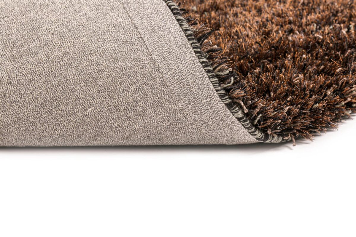Een close-up van het New Paulo Anthracite mix 770 vloerkleed in 170x230, gedeeltelijk gevouwen om de getextureerde, antisliprug tegen een wit oppervlak te laten zien.