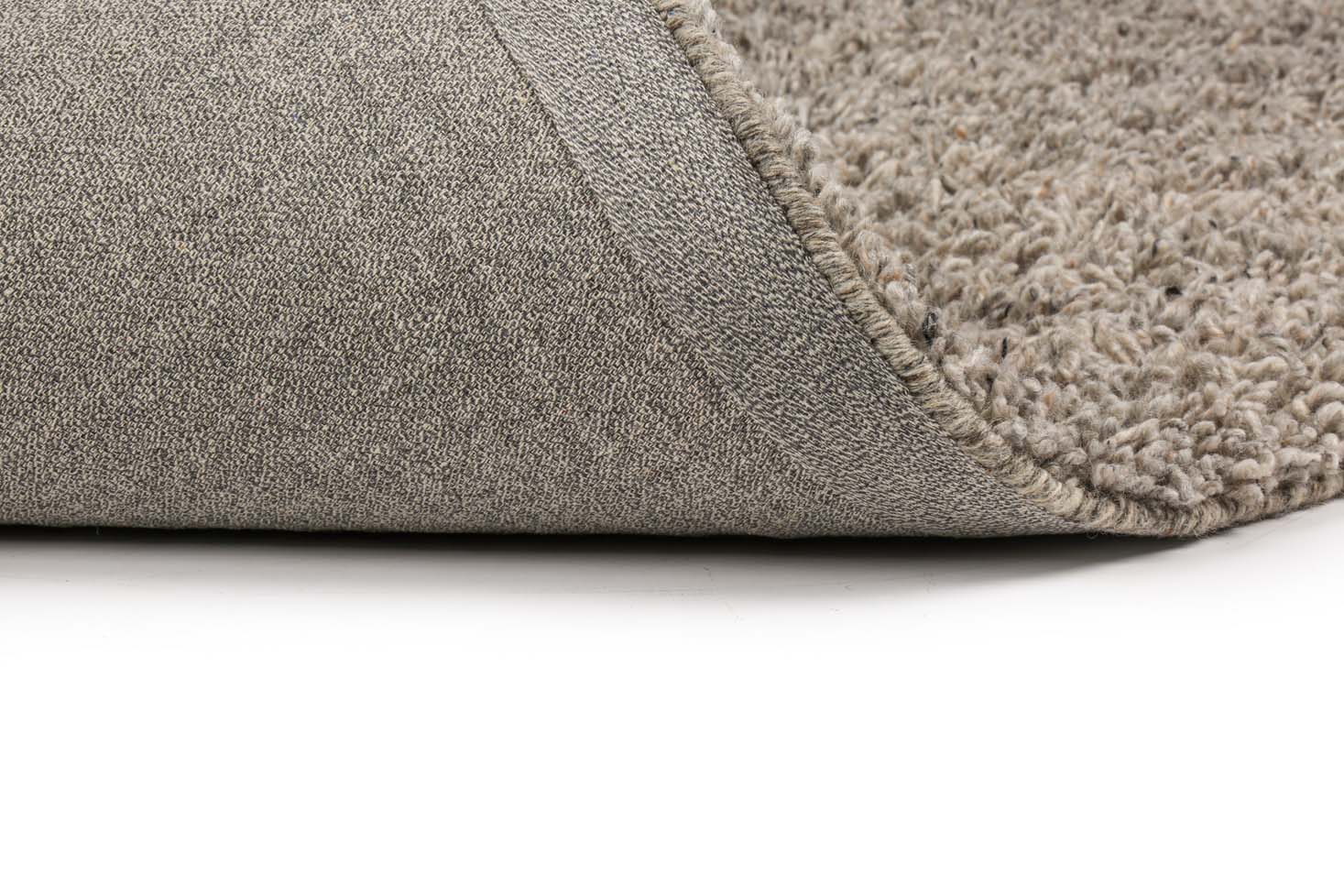Een close-up van het Berbero Lungo Natural Grey 834 170x230 tapijt, met een hoek opgetild om het gestructureerde oppervlak en de rug te onthullen, tegen een witte achtergrond.
