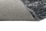 Een close-up van het New Paulo Grey Blue 211 170x230 tapijt toont een omgedraaide hoek, waardoor de gestructureerde stoffen achterkant en de dikke, zachte grijsblauwe pool zichtbaar worden.