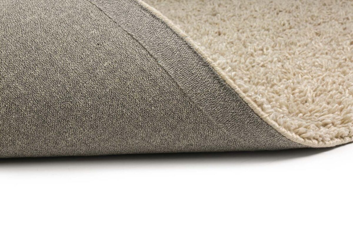 Een close-up van het Berbero Lungo Cloud White 815 170x230 beige tapijt, met het oppervlak met textuur en een opgelichte hoek om de antislip grijze tapijtrug op een witte ondergrond te onthullen.