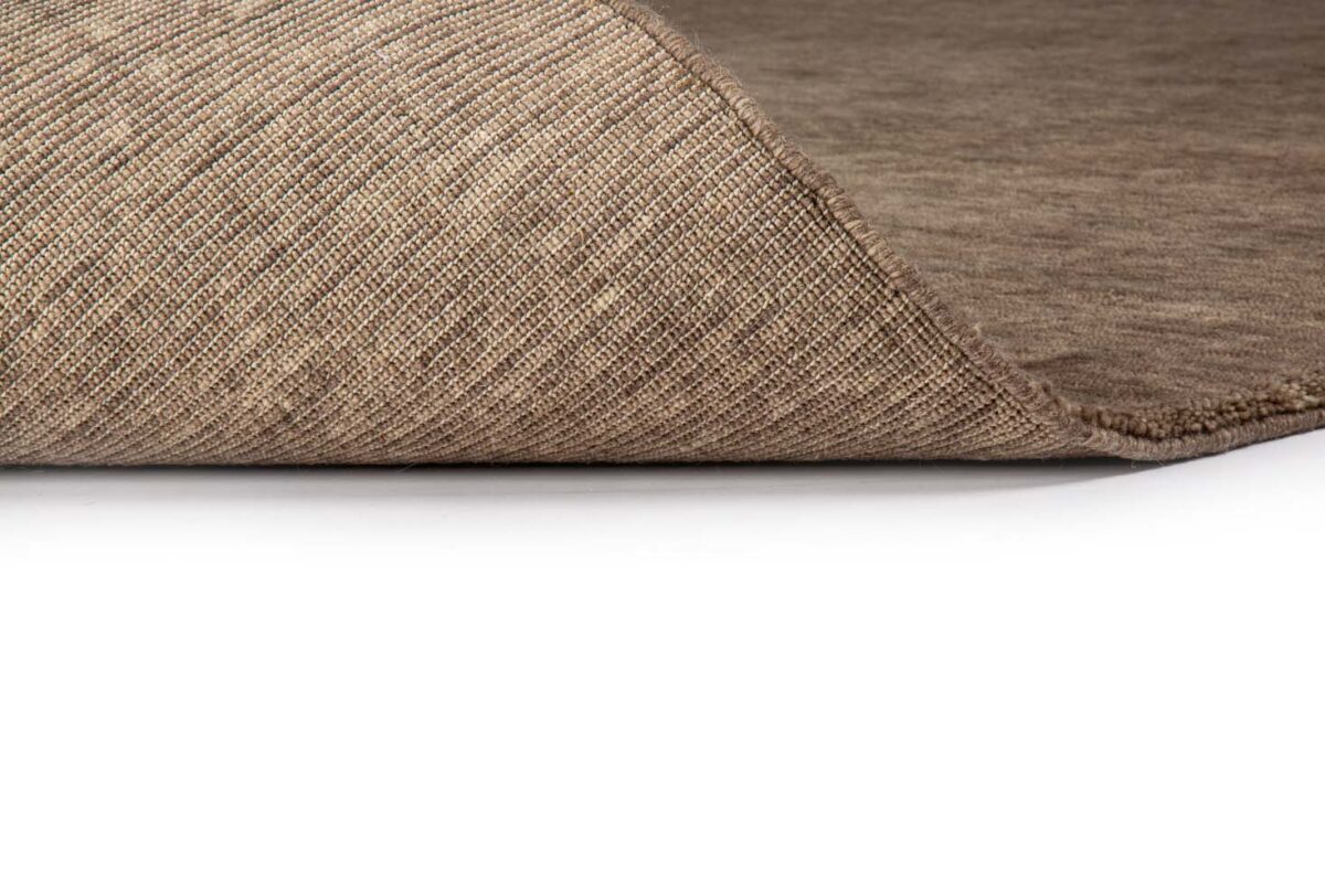 Een close-up van het San Stefano Camel 09 200x300 tapijt, met een bruin gestructureerd oppervlak waarvan één hoek iets is opgetild om de geweven onderkant te onthullen tegen een witte achtergrond.