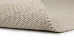 Een close-up van het Verona ST Cloud White 815 200x300 tapijt toont de lichtbeige, grof geweven textuur met een hoek gevouwen om de onderkant te onthullen.