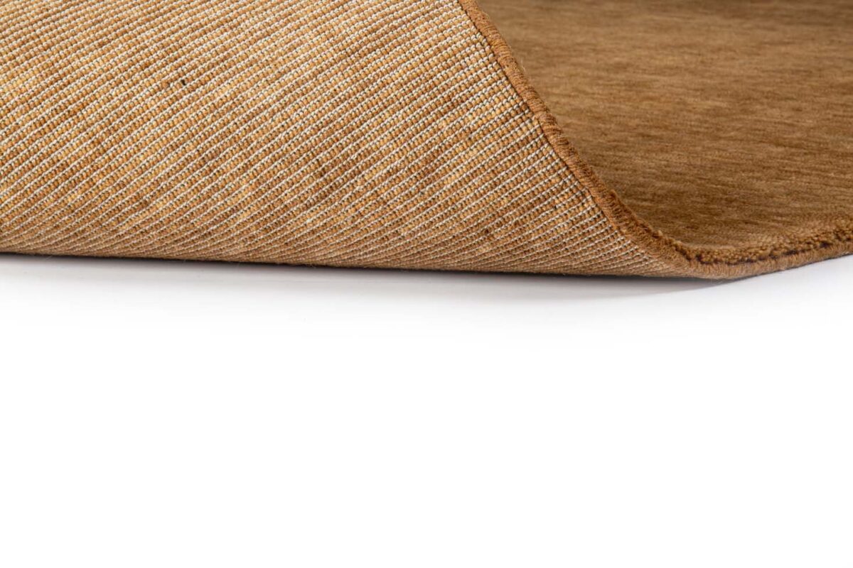 Een close-up van de hoek van het bruine vloerkleed San Stefano Rust 10 200x300, gedeeltelijk omgedraaid om de getextureerde onderkant te onthullen, tegen een witte achtergrond.