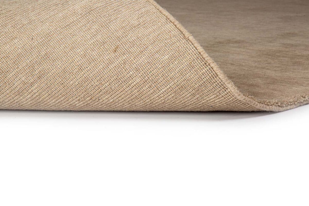 Een close-up van de zijkant van het San Stefano Light Beige 07 200x300 tapijt met een hoek omgevouwen, waardoor de geweven textuur en dikte goed uitkomen tegen een witte achtergrond.
