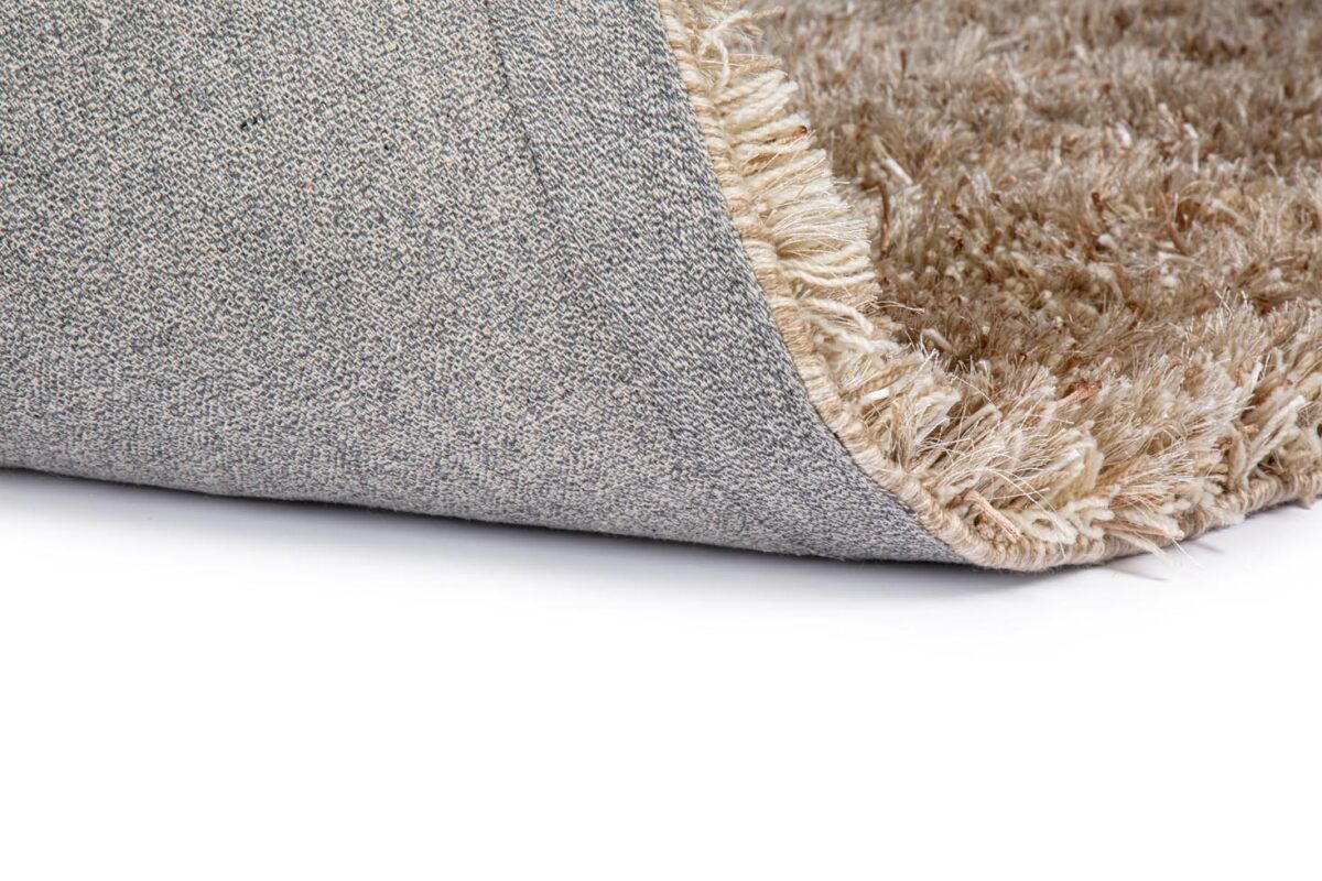 Close-up van de hoek van het New Paulo Light Beige mix 126 200x300 tapijt, opgetild om het beige-bruine shaggy oppervlak en de grijs geweven rug tegen een witte achtergrond te onthullen.