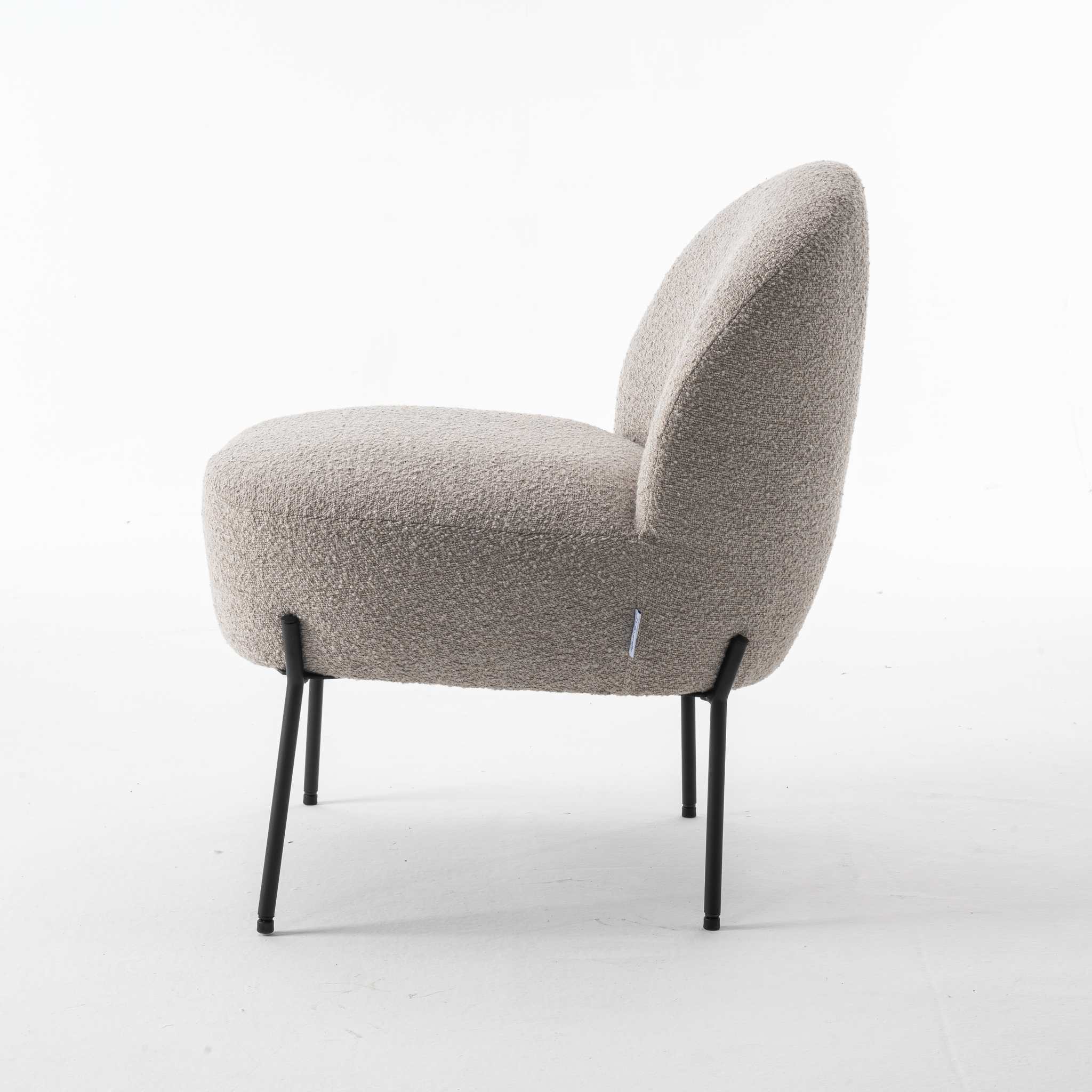 De Baudin fauteuil Stof Teddy Natural 01 is een moderne fauteuil met pluche, gestructureerde lichtbeige bekleding en slanke zwarte metalen poten, vanaf de zijkant afgebeeld tegen een effen witte achtergrond.