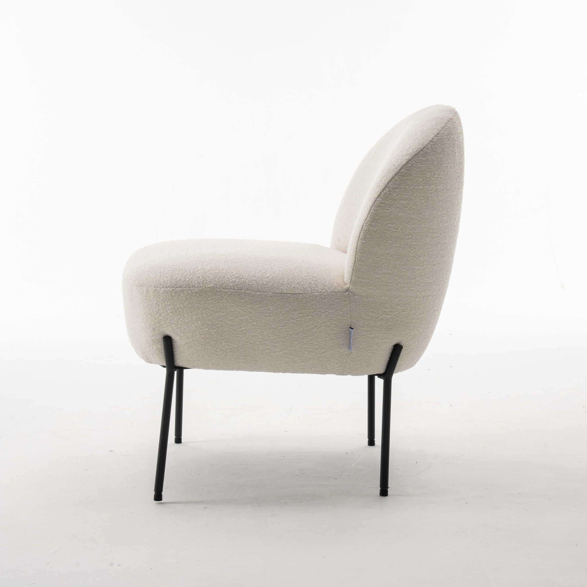 De Baudin fauteuil Stof Teddy Ivory 101 is een moderne, armloze loungestoel met ivoorkleurige bekleding en slanke zwarte metalen poten, van opzij gezien op een effen witte achtergrond.