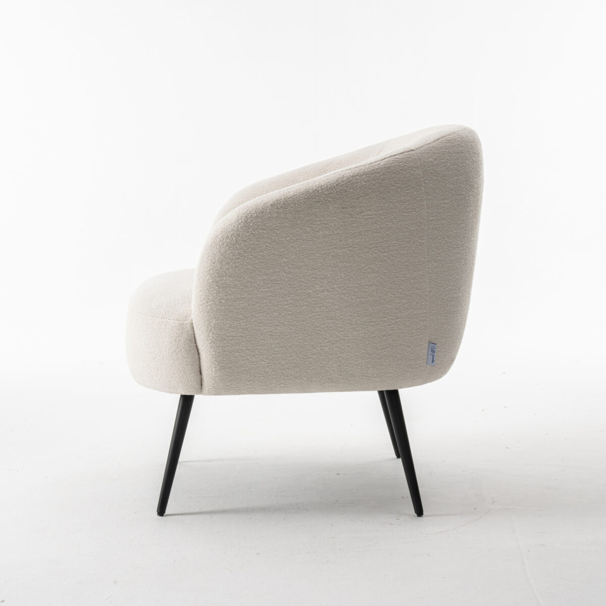 De Laura fauteuil Stof Teddy Ivory 101 is een moderne crèmekleurige accentstoel met een afgeronde rugleuning en zwarte metalen poten, van opzij gezien op een witte achtergrond.