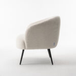 De Laura fauteuil Stof Teddy Ivory 101 is een moderne crèmekleurige accentstoel met een afgeronde rugleuning en zwarte metalen poten, van opzij gezien op een witte achtergrond.