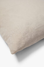 Een close-up van het Sierkussenhoes Scotty Taupe 50x50 cm, een beige kussenhoes met een zachte textuur, getoond op een wit oppervlak.