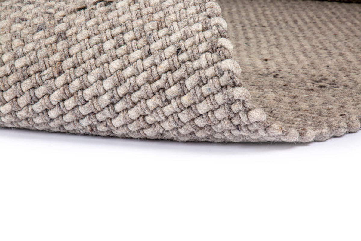 Close-up van het Burano Dark Grey 618-613 200x300 tapijt, met dikke, stevige vezels in een basketweave patroon op een witte ondergrond. Eén hoek is opgetild om de getextureerde onderkant te onthullen.