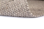 Close-up van het Burano Dark Grey 618-613 200x300 tapijt, met dikke, stevige vezels in een basketweave patroon op een witte ondergrond. Eén hoek is opgetild om de getextureerde onderkant te onthullen.