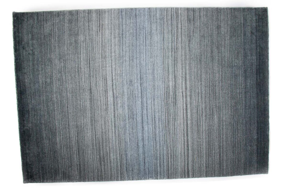 Het Portofino Blue 01 200x300 vloerkleed heeft een rechthoekige vorm met een patroon dat verloopt van donkerblauw aan de randen naar lichter blauw in het midden, geaccentueerd door subtiele verticale lijnen.