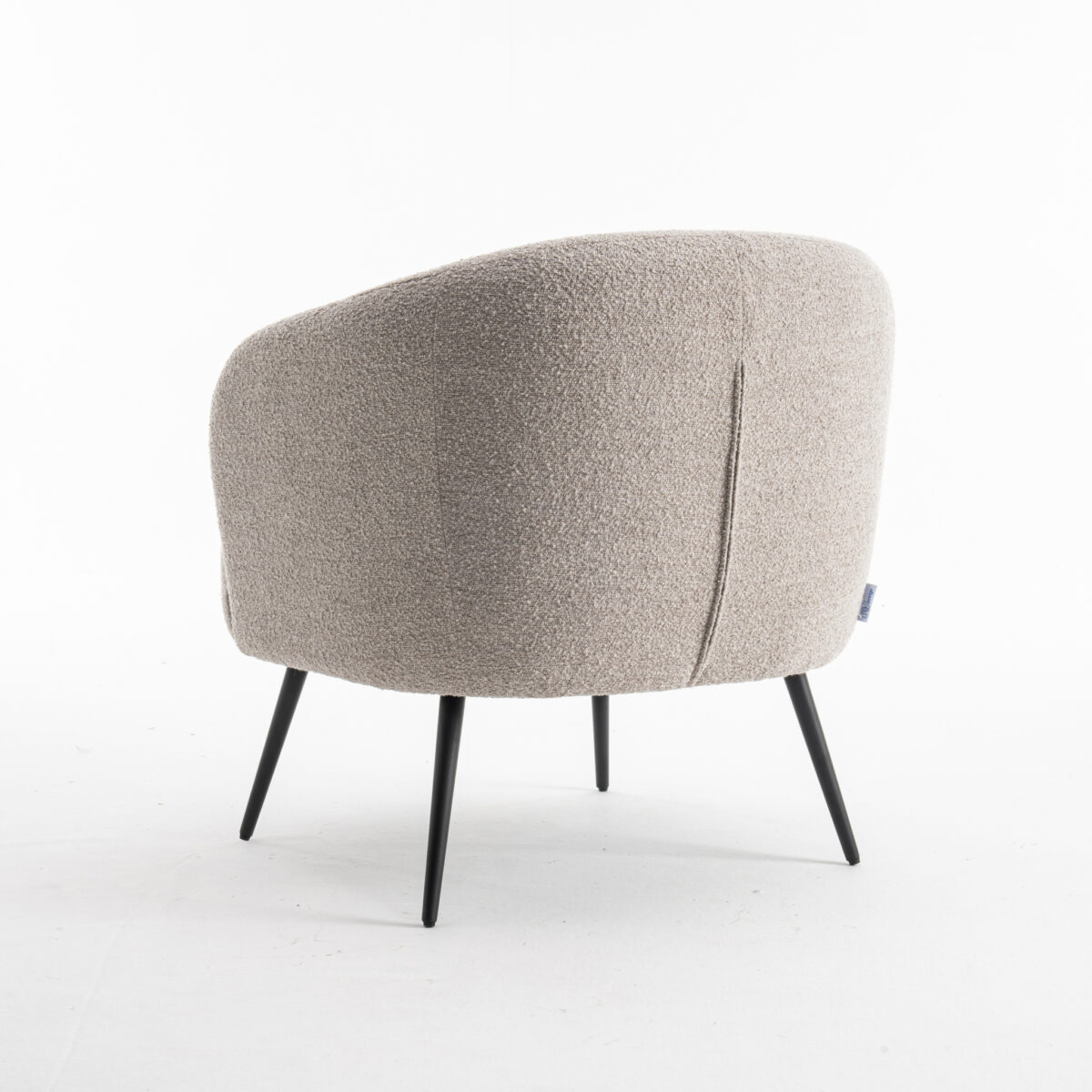 De Laura fauteuil Stof Teddy Natural 01 is een moderne beige fauteuil met een gestructureerde afwerking, ronde rugleuning en slanke zwarte metalen poten, tegen een effen witte achtergrond.