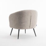 De Laura fauteuil Stof Teddy Natural 01 is een moderne beige fauteuil met een gestructureerde afwerking, ronde rugleuning en slanke zwarte metalen poten, tegen een effen witte achtergrond.