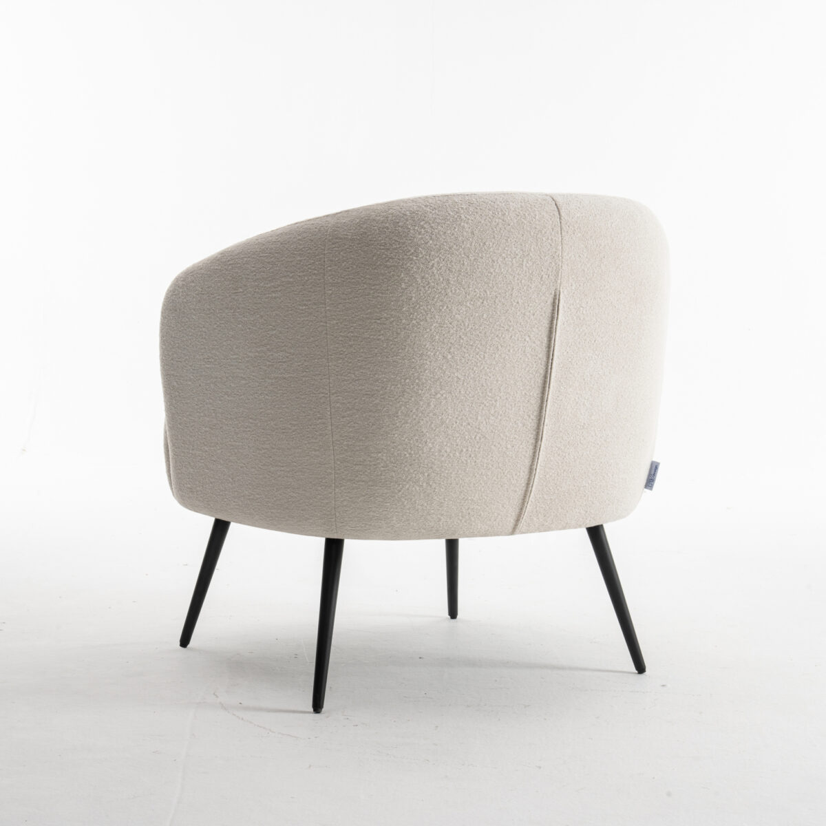 De Laura fauteuil Stof Teddy Ivory 101 is een moderne accentstoel met licht ivoorkleurige bekleding, een gebogen rugleuning en slanke zwarte poten, afgebeeld op een witte achtergrond.