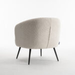 De Laura fauteuil Stof Teddy Ivory 101 is een moderne accentstoel met licht ivoorkleurige bekleding, een gebogen rugleuning en slanke zwarte poten, afgebeeld op een witte achtergrond.