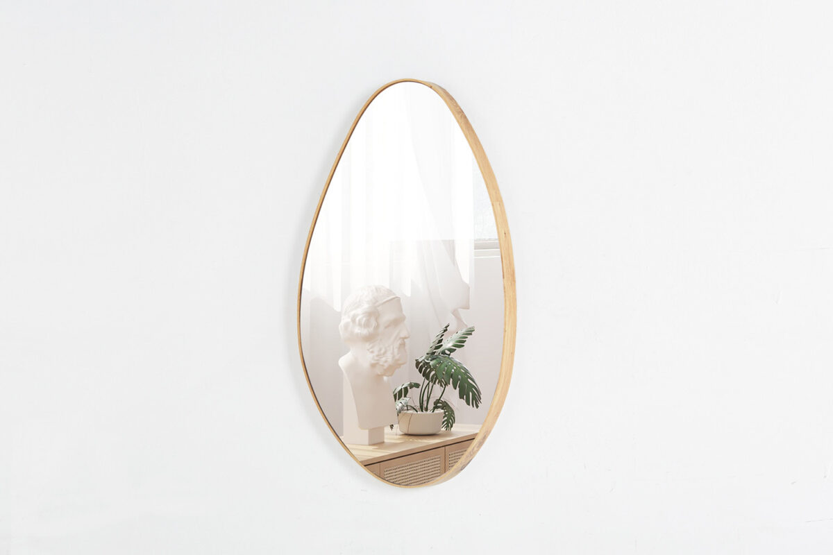 De Spiegel 'Romi' 80x50 Oude eik (1c), een ovale spiegel met een houten lijst, hangt aan een witte muur en weerspiegelt een wit borstbeeld, een groene potplant en transparante gordijnen in een minimalistische kamer.