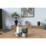 Een moderne eetkamer met een houten tafel gestyled met een brandende kaars, een kleine plant en structuurvazen. Op de achtergrond staat een dressoir met de Table Mirror, een vaas en abstracte zwart-wit muurkunst.