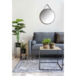 Een moderne woonkamer met een grijze bank, houten salontafel met twee potplanten, vloerkleed met patroon, vloerplant en de Trapani spiegel (zwart stalen frame, PU band, Ø60 cm) boven de bank.