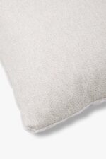 Een close-up van het Mohair sierkussenhoes Amy lichtgrijs 50x50 cm toont de lichtgrijze structuurstof, met een accent op één hoek met zichtbare randstiksels tegen een witte achtergrond.