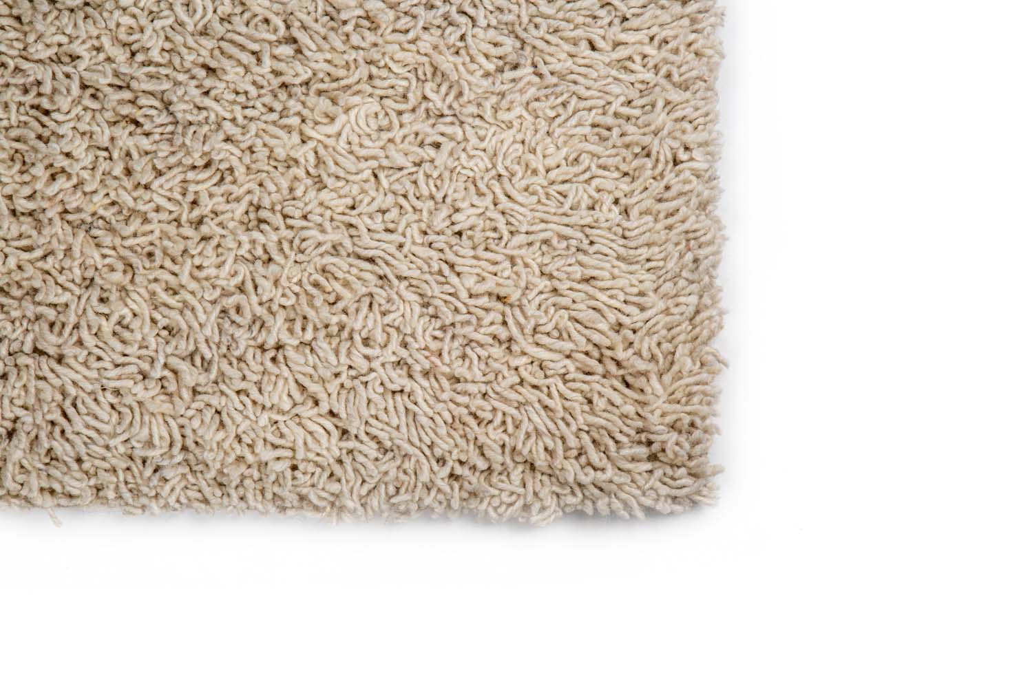 Een close-up toont de hoek van het Berbero Lungo Cloud White 815 200x300 tapijt, met dikke, gedraaide vezels en een beige, getextureerde shaggy look op een witte ondergrond voor een zacht, knus gevoel.