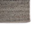 Close-up van de hoek van het Bressano Grey 834 200x300 tapijt, met een gestructureerd patroon van grijze en beige draden tegen een witte achtergrond.