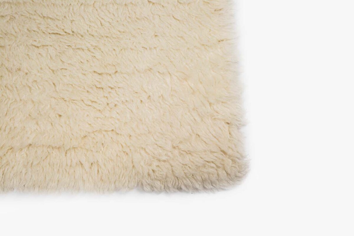 Close-up van de hoek van het Merano White 011 170x230 tapijt, met de zachte, pluizige off-white shaggy textuur tegen een effen witte achtergrond.